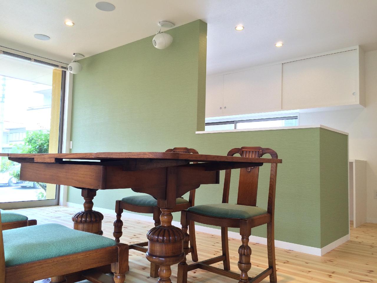 藤沢・鵠沼海岸　三角形変形敷地に建つ　ビーチハウス　箱の家 アンティークのダイニングテーブルと椅子。座面のファブリックの色と同系色のグリーン系の壁